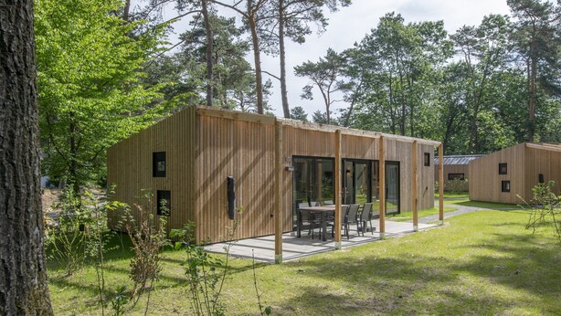 En moderne træhytte med terrasse, omgivet af træer.