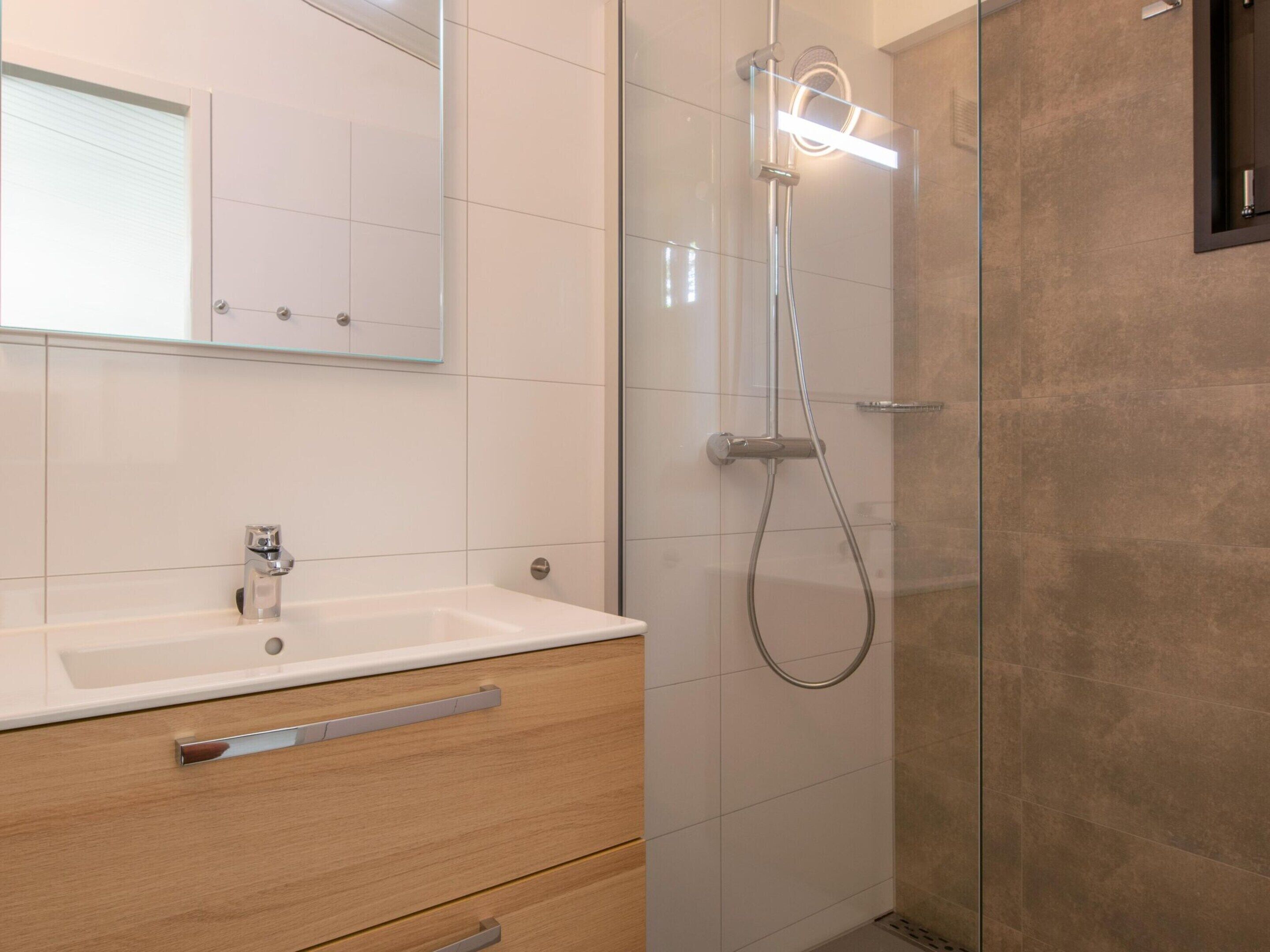 A modern bathroom with a white sink, wooden vanity, and a glass-enclosed shower area.