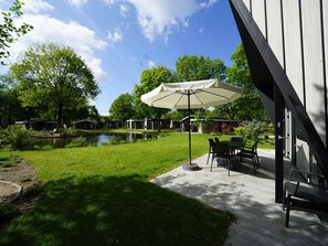 A patio area with a table and chairs, a large umbrella, and a pond. - Contemporary Chalet, Near De Efteling (Kaatsheuvel)