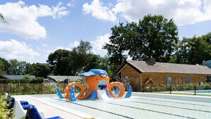 A swimming pool area with a large octopus water feature, a wooden building, and a fenced area with blue and white chairs. - Contemporary Chalet, Near De Efteling (Kaatsheuvel)