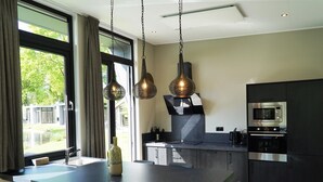 A modern kitchen with a large island, stainless steel appliances, and pendant lighting. - Contemporary Chalet, Near De Efteling (Kaatsheuvel)