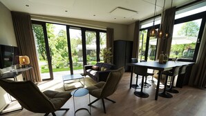 A modern living room with a sofa, chairs, a coffee table, and a dining area with a table and chairs. Large windows provide a view of the outdoors. - Contemporary Chalet, Near De Efteling (Kaatsheuvel)
