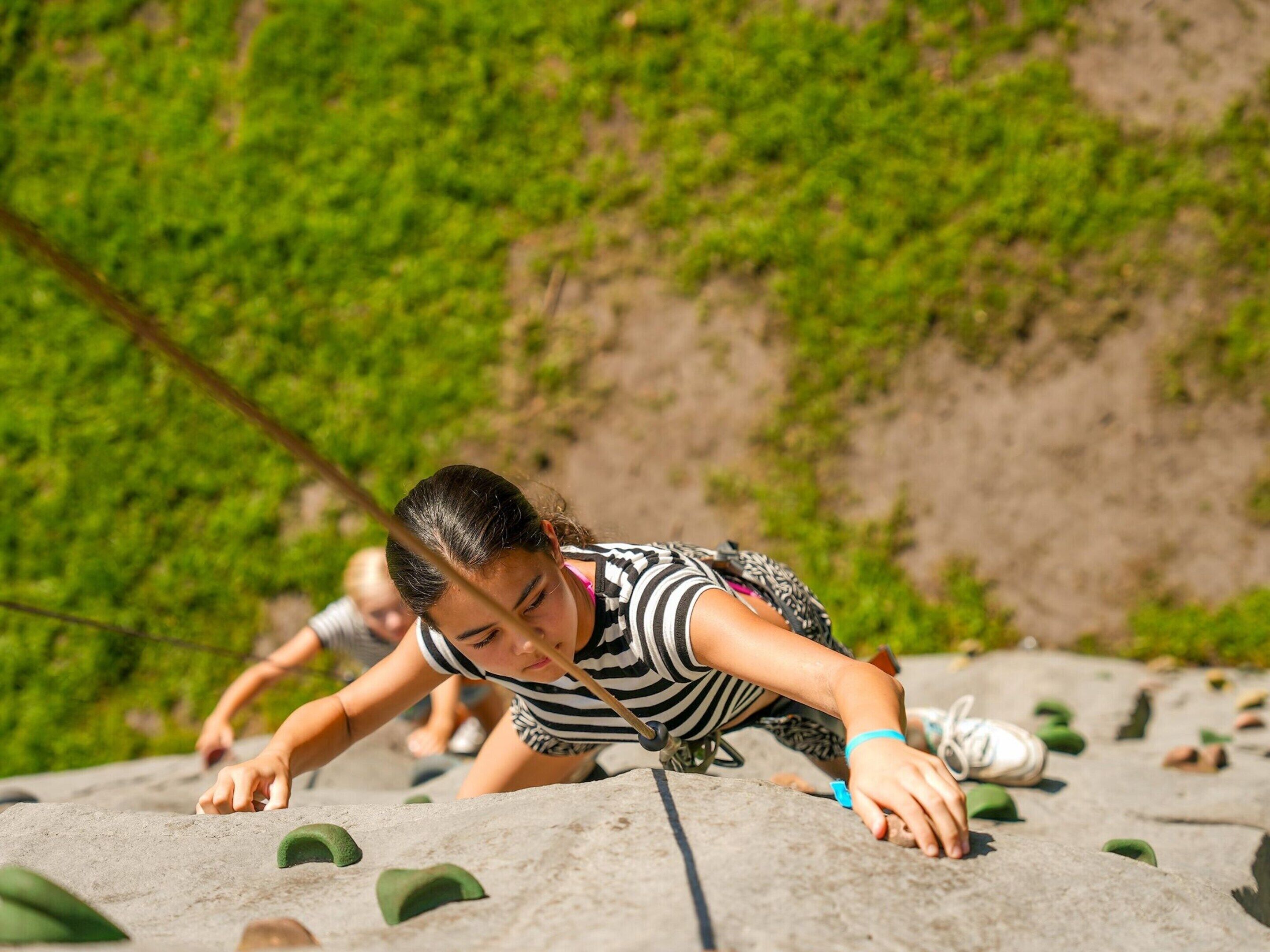 A person climbing a rock wall with green footholds.