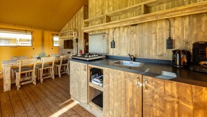 A kitchen with wooden cabinets, a gas stove, a sink, and a coffee maker. - Charming Safari Tent by the Lake (Gasselternijveen)