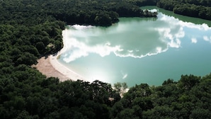 An aerial view of a lake surrounded by dense forest, with a sandy beach area visible on one side. - Charming Safari Tent by the Lake (Gasselternijveen)