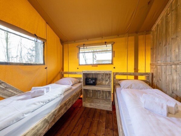 A cabin with two wooden bunk beds, a small wooden shelf with a radio, and a window with a view of trees.