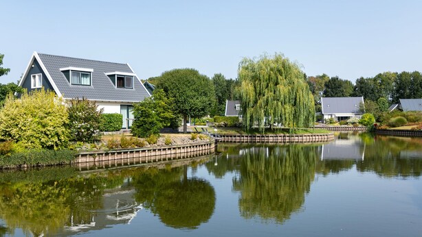 A tranquil residential area with houses, a pond, and a weeping willow tree. - Charming Safari Tent by the Lake (Gasselternijveen)
