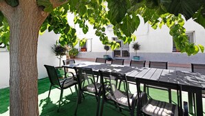An outdoor patio with a table and chairs, surrounded by greenery and a white building.