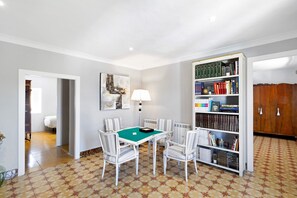 Ein Zimmer mit einem grünen Tisch, gestreiften Stühlen, einem Bücherregal und einem Holzschrank.