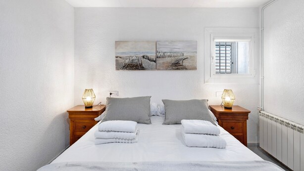 A bedroom with a bed, two nightstands, two lamps, a window, and two wall art pieces.