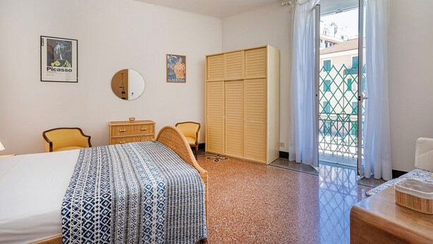 A hotel room with a bed, two chairs, a wooden wardrobe, a small table, and a window with curtains. - Classy Apartment in Rapallo by Wonderful Italy (Rapallo)