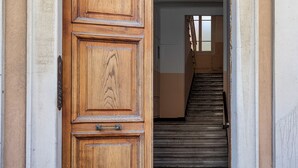 A wooden door with a metal handle and a metal plate, leading to a staircase with a metal railing. - Classy Apartment in Rapallo by Wonderful Italy (Rapallo)