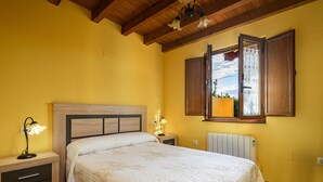 Ein Schlafzimmer mit hölzernem Kopfteil, einem Bett mit weißer Bettdecke, einem Nachttisch mit Lampe und einem Fenster mit Vorhängen.