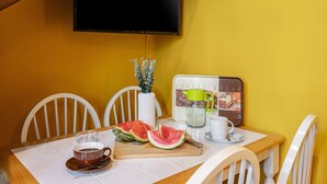 Ein Esstisch mit weißer Tischdecke, einer Kaffeetasse, einem Teller mit Wassermelonenstücken, einer Karaffe und einer weißen Vase mit Blumen.