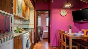 A kitchen with wooden cabinets, a washing machine, a dining table with chairs, a television, and a clock on the wall. - Country House 'Apartamento Rosa' with Shared Garden (Susacasa)
