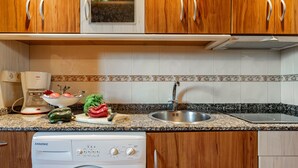 A kitchen with wooden cabinets, a built-in oven, a dishwasher, a sink, and a countertop with various kitchen items. - Country House 'Apartamento Rosa' with Shared Garden (Susacasa)