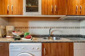 A kitchen with wooden cabinets, a built-in oven, a dishwasher, a sink, and a countertop with various kitchen items. - Country House 'Apartamento Rosa' with Shared Garden (Susacasa)