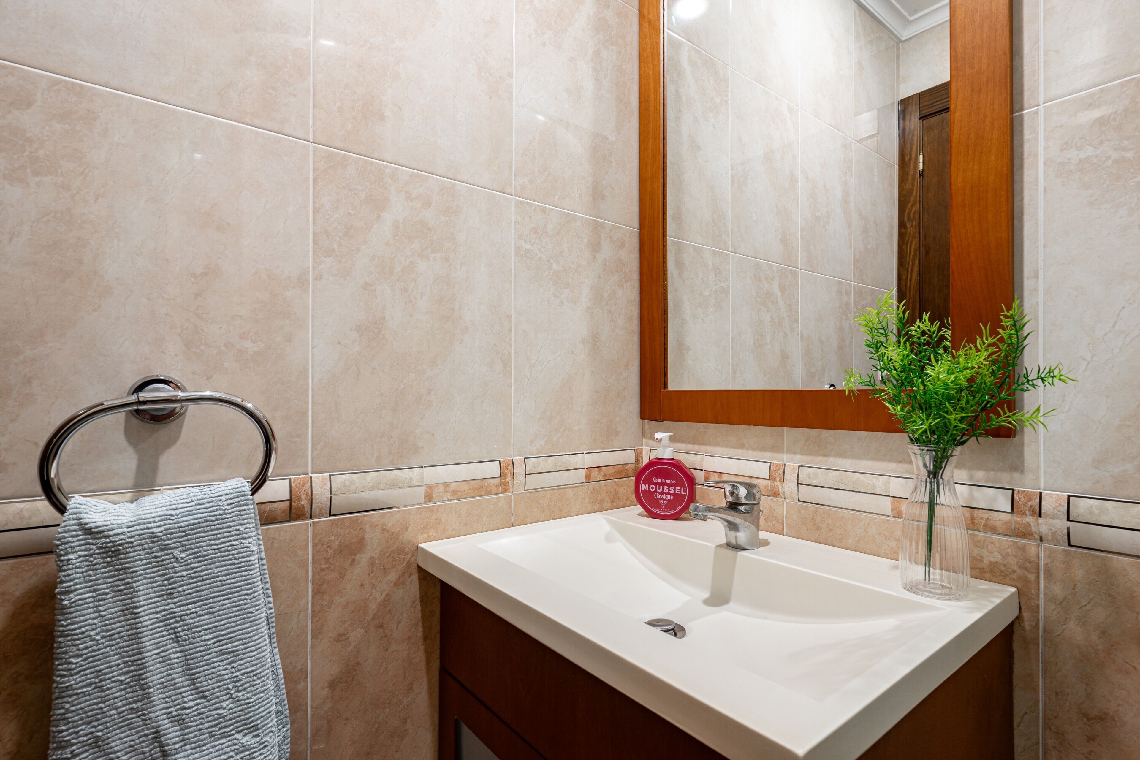 A bathroom with a white sink, a mirror, a towel rack, and a potted plant.