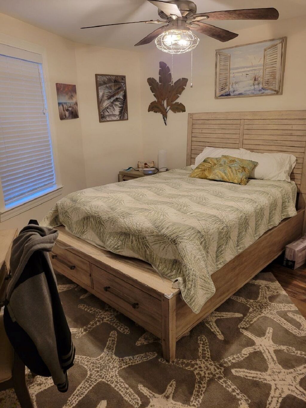 A bedroom with a bed, a ceiling fan, a nightstand, and a wall with framed pictures.