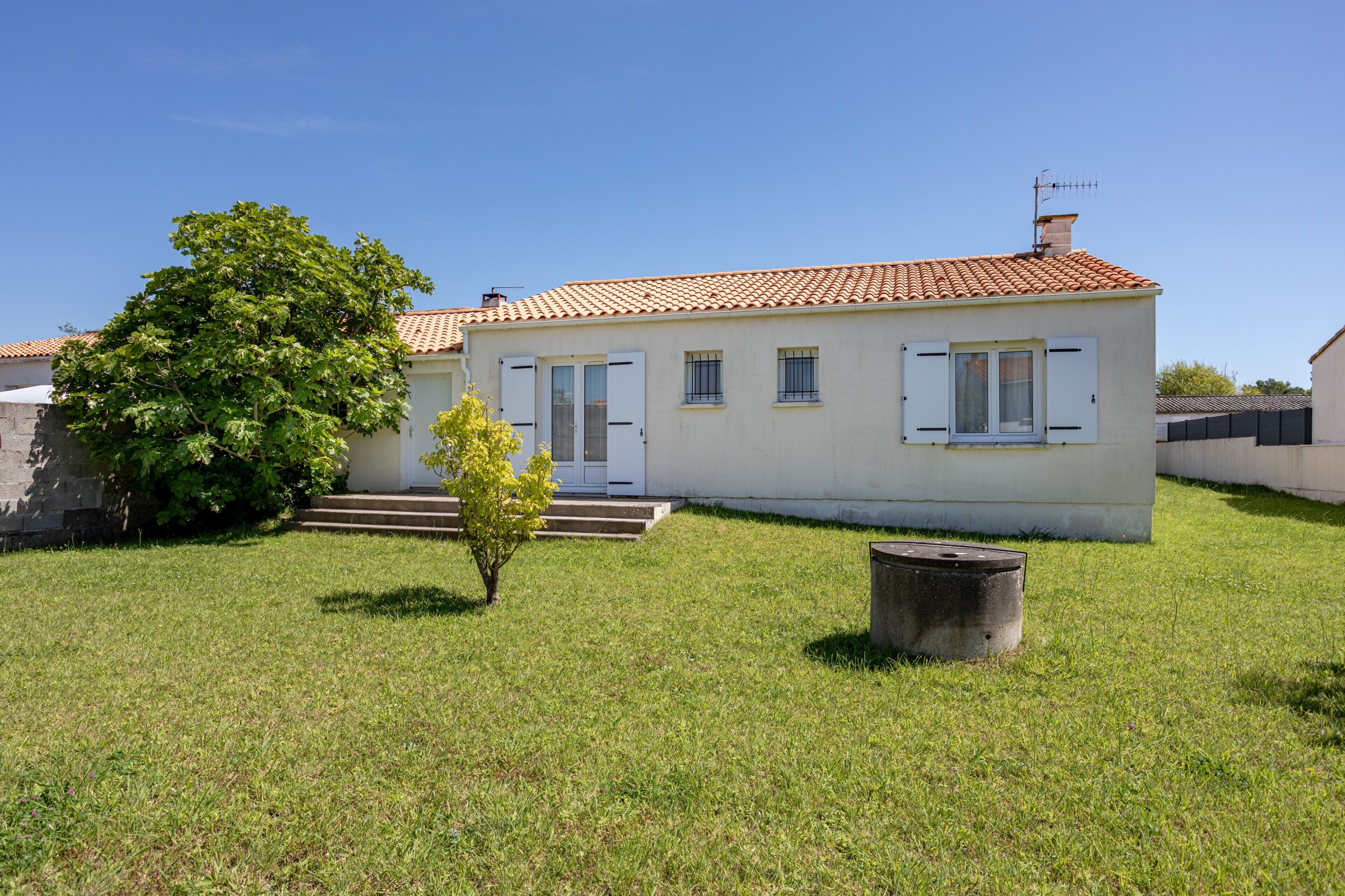 A two-story house with a tiled roof, a small front yard, and a tree.
