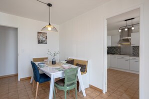 Zona pranzo con tavolo, sedie, lampadario e cucina visibile attraverso un'apertura.