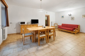 Ein Zimmer mit einem Holzesstisch, Stühlen, einem Fernseher, einem roten Sofa und einem Holzkabinett.