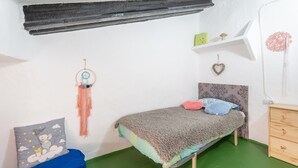 Ein kleines, ordentlich eingerichtetes Schlafzimmer mit einem Einzelbett, einem blauen Sitzsack, einem Traumfänger und einem kleinen Regal mit Dekoration.
