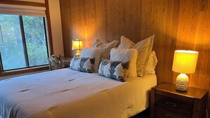 A bedroom with a large bed, multiple pillows, a nightstand with a lamp, and a window with a view of trees. - Walk to Village!  Clean 2BDRM Palisades Tahoe Condo: Hikes, Dining, Wifi (Olympic Valley)
