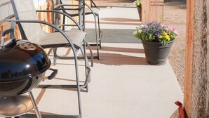 Une terrasse extérieure couverte, équipée d’un barbecue, de sièges et d’une plante en pot.