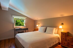 Ein Schlafzimmer mit einem Bett, Nachttischlampen, einem Schreibtisch mit Lampe, einem Fenster und einem Nachttisch.