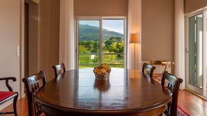 Un comedor con una mesa redonda, sillas, un cesto de flores y vistas al verdor a través de un ventanal.