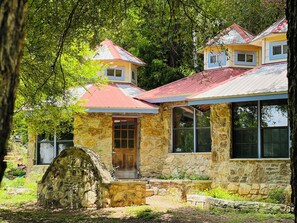 A stone house with a red roof, large windows, and a stone staircase leading to the entrance.