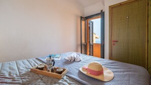 Un dormitorio con una cama, una bandeja de madera con una cafetera y un sombrero de paja.
