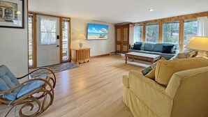 A spacious living room with a wooden floor, a sofa, a rocking chair, a coffee table, and a painting on the wall.