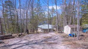 A rustic cabin with a dirt ground, surrounded by tall trees and a clear sky.