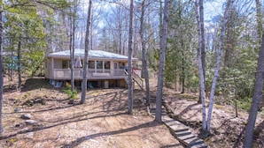 A cabin with a porch and a staircase leading up to it, surrounded by trees.