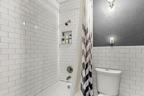 Een moderne badkamer met witte metro tegels, een douche met een handdouche, een toilet en een plank met toiletartikelen.