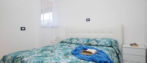 Ein Schlafzimmer mit einem Bett, einem Nachttisch, einem Fenster mit Vorhängen und einer Wandklimaanlage.