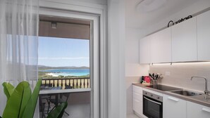 A modern kitchen with white cabinets and a view of the sea through a balcony. - Harenae Beach Gateway by Wonderful Italy (Olbia)