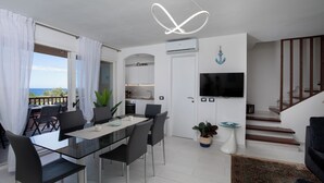 A modern living room with a dining area, a staircase, and a view of the outdoors. - Harenae Beach Gateway by Wonderful Italy (Olbia)