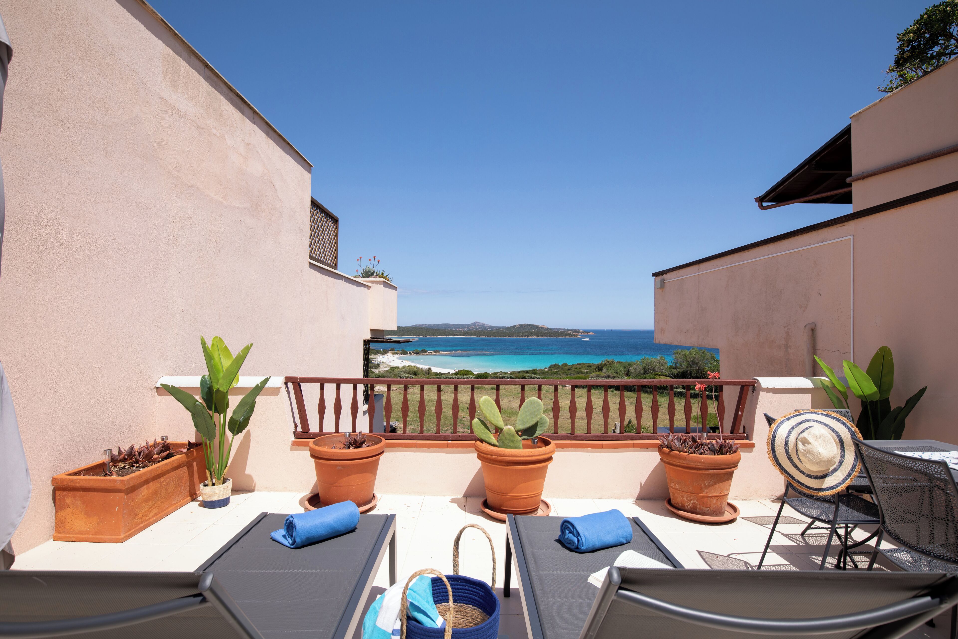 A balcony with two sun loungers, a table, and potted plants.
