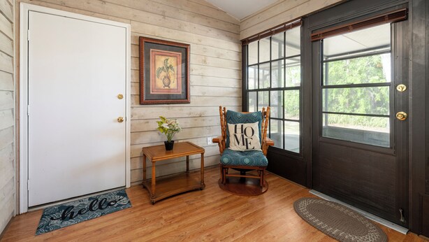 A wooden interior with a door, a rocking chair, a small table with a plant, and a window with a view. - New King Bed in spacious Ridge Manor Villa with BBQ, Screened Lanai, and Views (Ridge Manor)