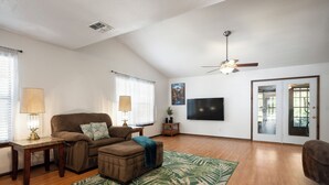 A living room with a sofa, ottoman, lamp, and a large flat-screen TV mounted on the wall. - New King Bed in spacious Ridge Manor Villa with BBQ, Screened Lanai, and Views (Ridge Manor)