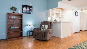 A living room with a recliner, a bookshelf, a lamp, and a painting on the wall. - New King Bed in spacious Ridge Manor Villa with BBQ, Screened Lanai, and Views (Ridge Manor)