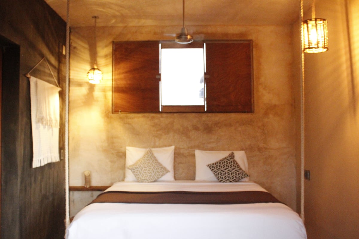 A bedroom with a bed, two wall-mounted lamps, a window, and a wooden headboard.