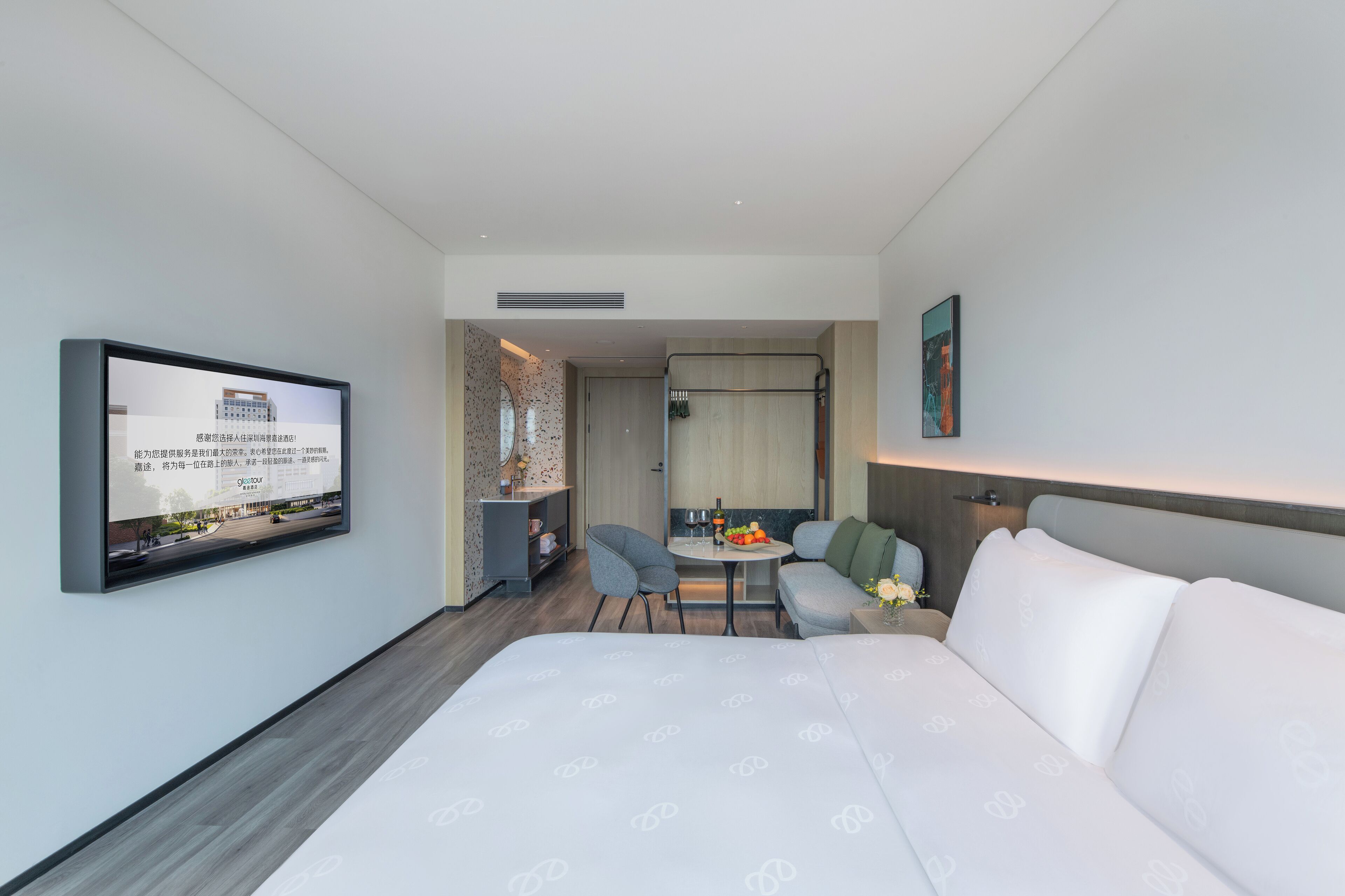 A modern hotel room with a large bed, a TV mounted on the wall, a small dining table with chairs, and a sofa.