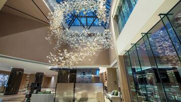 A spacious lobby with a high ceiling, modern furniture, and a large glass wall offering a view of the cityscape.