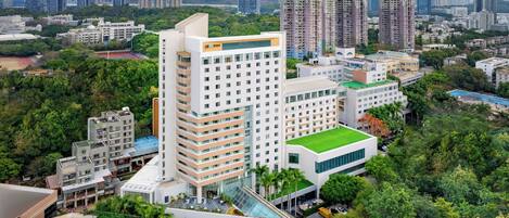 A high-rise hotel with multiple floors, a rooftop pool, and surrounding greenery.