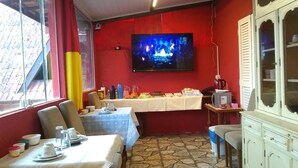 A dining area with a TV mounted on the wall, a table set with plates and glasses, and a cabinet with glass doors. - Casa da Dine (Campos do Jordão)