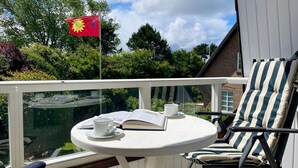 A balcony with a table, chairs, a flag, and a view of greenery.